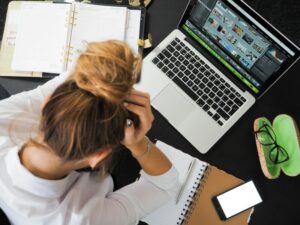 Overhead view of a stressed woman working at a desk with a laptop, worried about financing acquisitions.