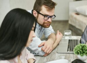 A man and woman sitting at a table reviewing business loans with no personal guarantee documents on a laptop indoors.