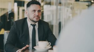 Man in suit talking across table with coffee.