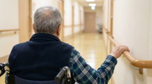 senior, elderly, wheelchair, corridor, hallway, nursing home, assisted living, railing, handrail, institutional, long-term care, patient, resident, plaid shirt, back view, aging, grey hair, perspective, medical, support, ai generated